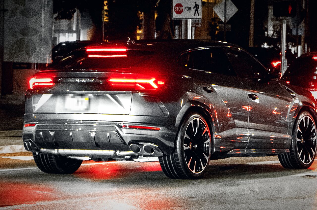 Traseira de um Lamborghini Urus cinza numa rua à noite, com as lanternas vermelhas acesas